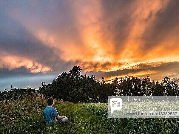 Mann sitzt im Gras und genießt den wunderschönen Sonnenuntergang und schaut in die Ferne