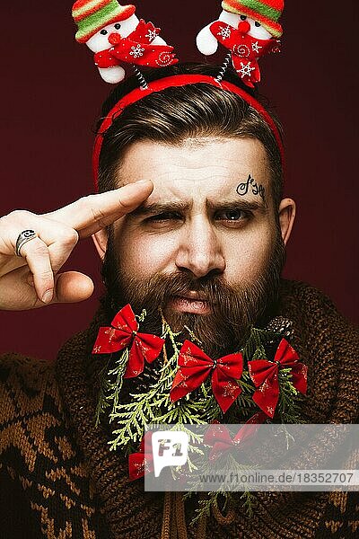 Lustiger bärtiger Mann in einem Neujahrsbild als Weihnachtsmann mit Dekorationen auf seinem Bart. Fest der Weihnacht. Fotos im Studio aufgenommen
