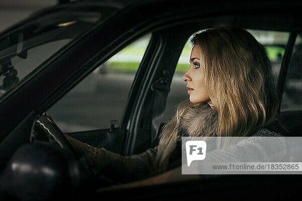 Stadtporträt einer hübschen blonden Fahrerin im Auto. Nachtszene. Dame hinter dem Steuer. Weichzeichner Foto  enthalten ein wenig Lärm