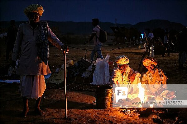 Indische Dorfbewohner und Kamele  die nachts am Lagerfeuer auf der Pushkar-Kamelmesse Pushkar Mela  der jährlichen berühmten Kamel- und Viehmesse und Touristenattraktion  Pushkar  Indien  Asien