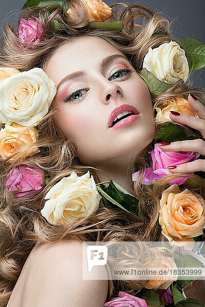 Schönes Mädchen mit vielen Blumen im Haar und leuchtend rosa Make-up. Frühling Bild. Schönheit Gesicht. Bild im Studio auf einem grauen Hintergrund aufgenommen