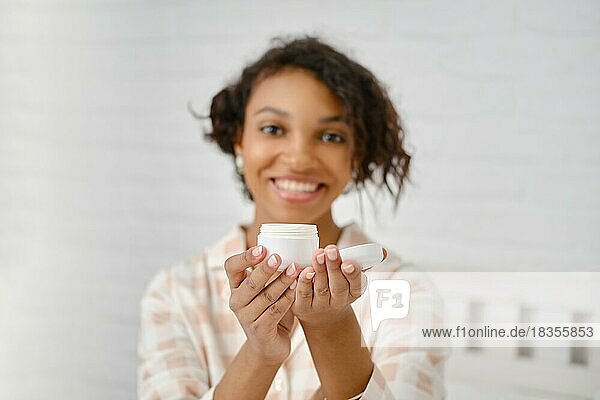 Lächelnde afroamerikanische Frau hält Hautcreme in den Händen (Fokus auf den Vordergrund)