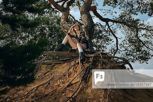 Attraktives Touristenmädchen  das auf der Wurzel eines Baumes sitzt und sich nach einem Spaziergang ausruht