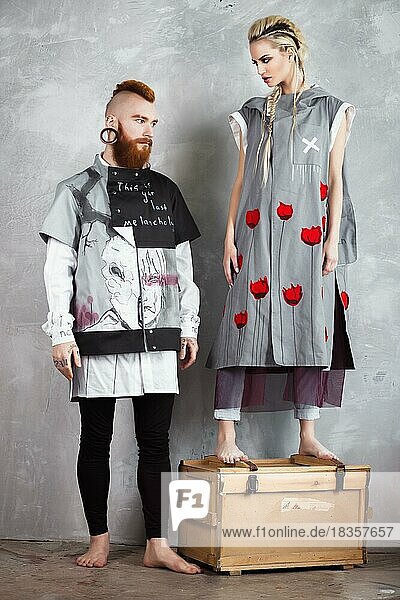 Kreatives ungewöhnliches blondes Mädchen und rothaariger Mann in Designerkleidung und mit Zöpfen auf dem Kopf posieren im Studio