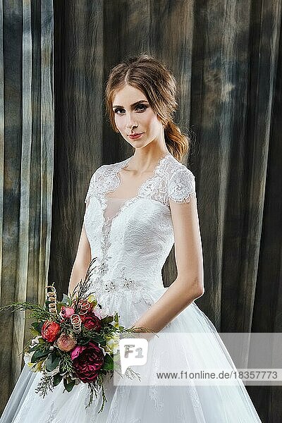 Portrait of pretty bride in wedding dress with flowers in hands
