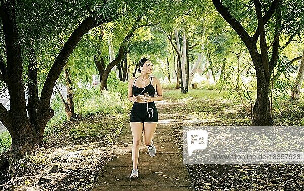 Lifestyle einer sportlichen jungen Frau  die in einem von Bäumen umgebenen Park läuft. Gesunder Lebensstil Konzept  Sportliche junge Frau läuft in einem Park. Ein Mädchen läuft in einem Park  während es Musik hört