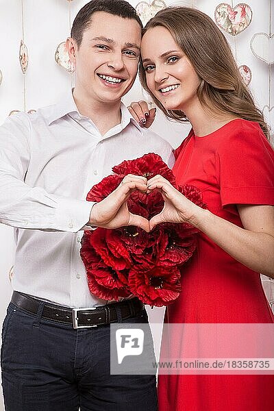 Schönes junges verliebtes Paar mit einem Blumenstrauß  der die Form von Herzhänden zeigt. Valentinstag. Bild im Studio aufgenommen