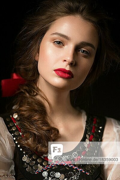 Schönes russisches Mädchen im Nationalkleid mit Zopffrisur und roten Lippen. Schönes Gesicht. Bild im Studio auf einem schwarzen Hintergrund genommen