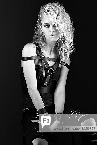 Gewagtes Mädchenmodell in schwarzem Lederkleid im Rock-Stil  dunkles Make-up  nasse Haare und Armbänder an den Armen. Das Bild wurde im Studio aufgenommen. Schwarz-Weiß-Bild