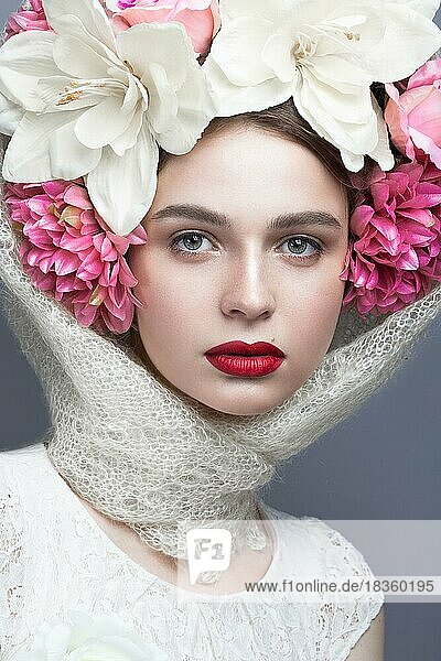 Schönes Mädchen mit einem Kopftuch im russischen Stil  mit großen Blumen auf dem Kopf und roten Lippen. Schönheit Gesicht. Bild im Studio auf einem grauen Hintergrund genommen