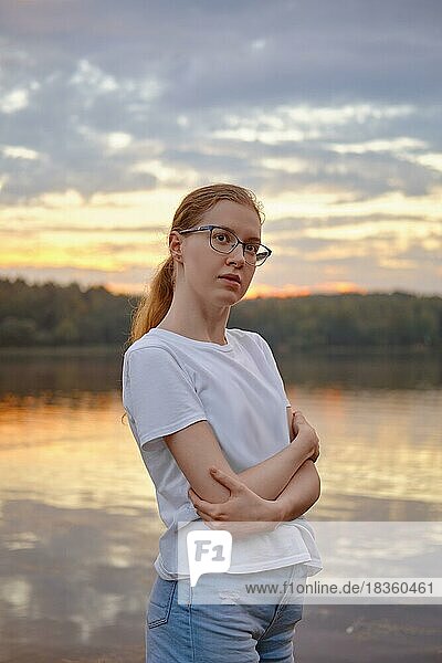 Young woman with crossed arms by the lake at sunset