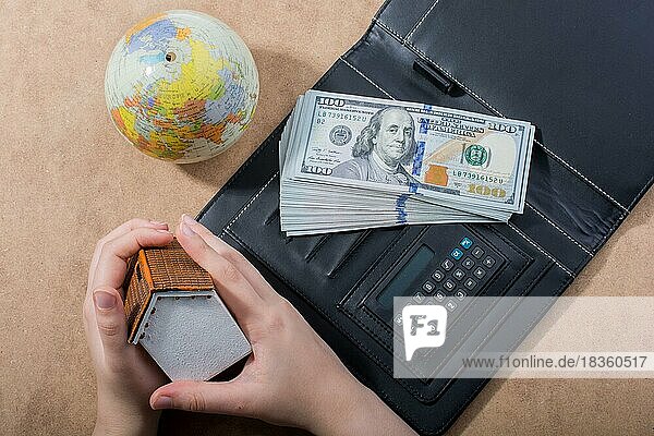 Hand hält Haus neben amerikanischen Dollar-Banknoten und Globus