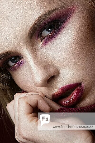 Schöne blonde Frau in einem roten Pullover mit hellem Make-up und dunklen Lippen. Schönes Gesicht. Foto im Studio aufgenommen. Porträt in Nahaufnahme