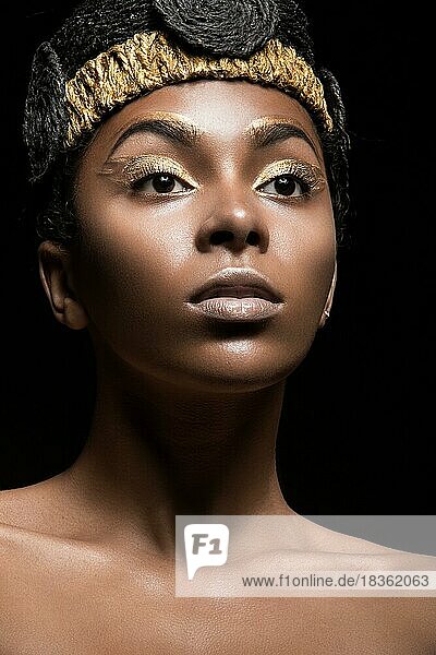 Afrikanisches Mädchen mit hellem Make-up und kreativen goldenen Accessoires auf dem Kopf. Schönes Gesicht. Bild im Studio auf einem schwarzen Hintergrund genommen
