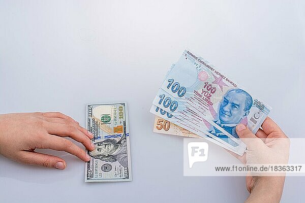 Hände halten amerikanische Dollar-Banknoten und Türkische Lira-Banknoten nebeneinander auf weißem Hintergrund