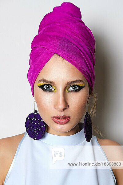 Porträt eines schönen Modemodells in tailliertem Kleid und Turban auf dem Kopf. Helles Make-up und große Ohrringe