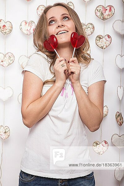 Valentinstag. Lustige schöne Frau hält Süßigkeiten in Form von Herzen. Schönheit Gesicht. Bild im Studio mit Dekorationen genommen