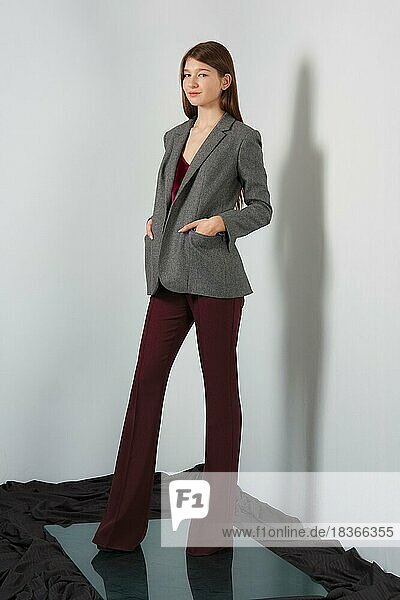 Attraktive Mode-Modell in Hosen  Bluse auf Trägern und Jacke posiert für Lookbook in der Nähe von grauen Wand