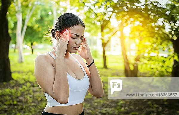 Junge Frau Läuferin reibt ihren Kopf mit Migräne in einem Park. Läuferin mit Kopfschmerzen und Müdigkeit im Park  Läuferin mit Kopfschmerzen im Park  Sportler Mädchen mit Migräne in einem Park