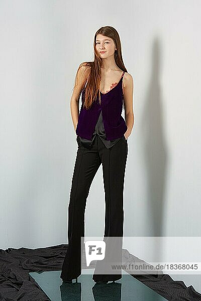 Attraktive Mode-Modell in Hosen und Bluse auf Riemen posiert für Lookbook in der Nähe von grauen Wand