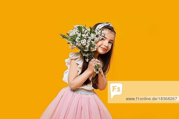 Fröhliches kleines Kind mit Frühlingsblumen in den Händen auf leuchtend gelbem Hintergrund