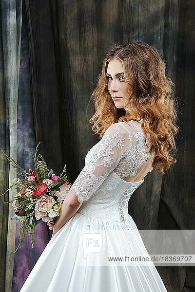Portrait of pretty bride in wedding dress with flowers in hand in profile
