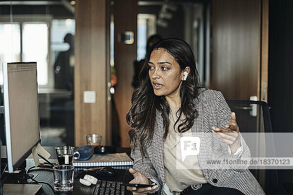Unternehmerin schaut auf den Computer  während sie im Büro mit ihrem Smartphone spricht