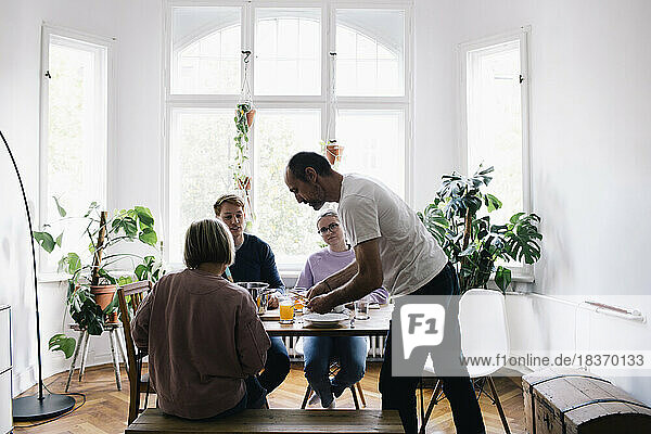 Side view of man serving juice to family on dining table at home