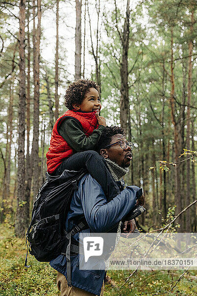 Side view of father carrying son on shoulder while exploring forest during vacation