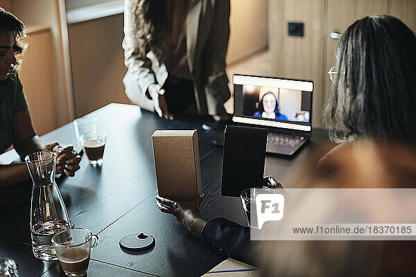 Geschäftsfrau zeigt einem Unternehmer während eines Videogesprächs im Büro einen Warenkasten