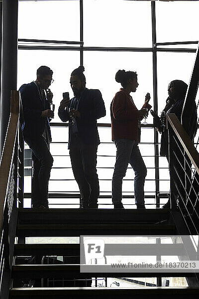 Multirassische männliche und weibliche Kollegen diskutieren miteinander auf einer Treppe bei einer Firmenveranstaltung