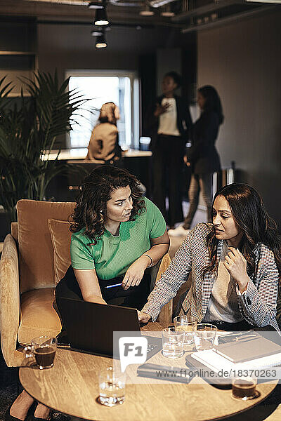 Multiracial businesswomen discussing over laptop while sitting at table in office