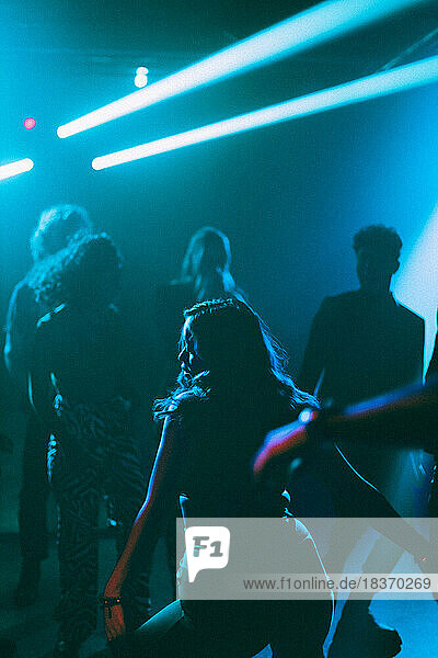 Rear view of young woman dancing near friends on dance floor at nightclub