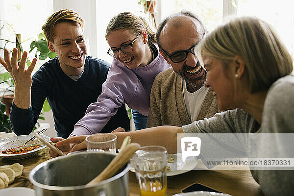 Glückliche Familie genießt die gemeinsame Mahlzeit  während sie sich zu Hause ein Smartphone teilt