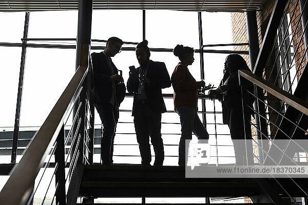 Multirassische männliche und weibliche Unternehmer diskutieren miteinander auf einer Treppe bei einer Firmenveranstaltung