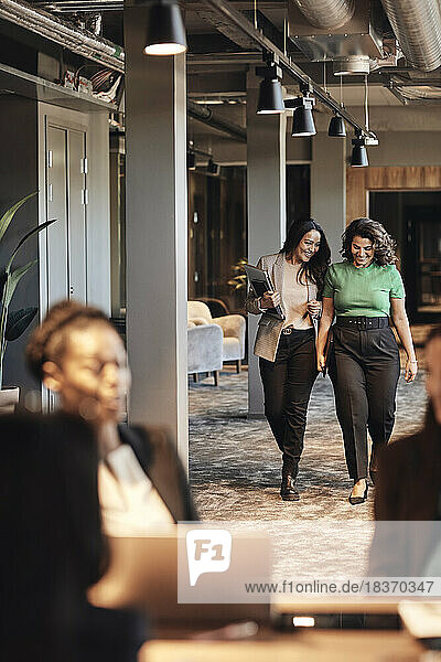 Happy female entrepreneurs walking and talking in office