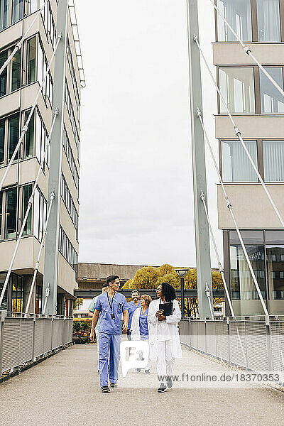 Eine gemischtrassige Gruppe von männlichen und weiblichen Mitarbeitern des Gesundheitswesens geht auf einer Brücke inmitten eines Krankenhausgebäudes spazieren