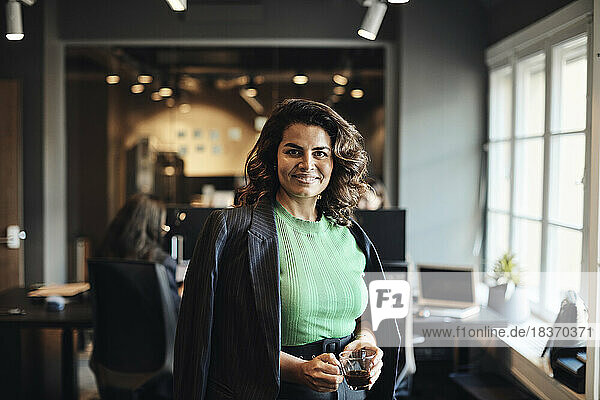 Portrait of happy female entrepreneur with tea cup standing at office