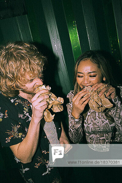 Young friends eating sandwich while enjoying at nightclub