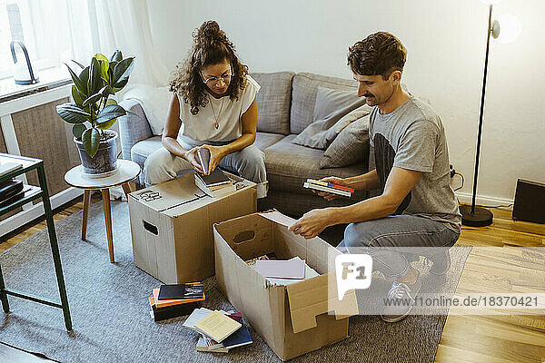 Boyfriend and girlfriend talking to each other while unboxing cardboard boxes in living room at home