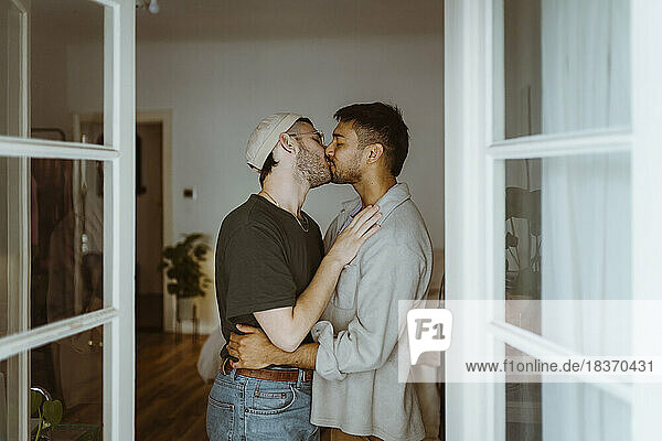 Seitenansicht eines romantischen schwulen Paares  das sich küsst  gesehen durch eine Türöffnung