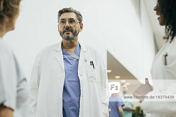 Reifer männlicher Arzt im Laborkittel diskutiert mit Kollegen im Krankenhaus