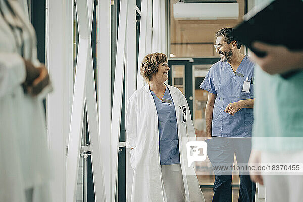 Mature male physician talking with female doctor while walking in corridor at hospital