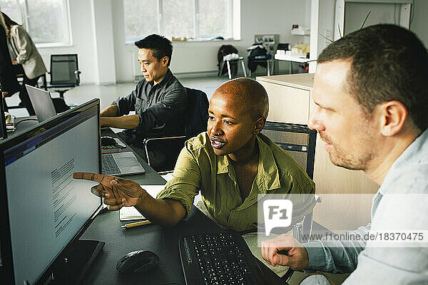 Geschäftsfrau  die auf einen Computer zeigt  während sie mit einem männlichen Kollegen im Büro diskutiert