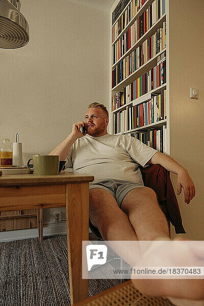 Man talking on mobile phone while sitting near bookshelf at home