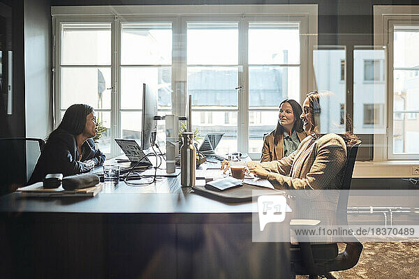 Multiracial female business colleagues discussing strategy while sitting at desk in office
