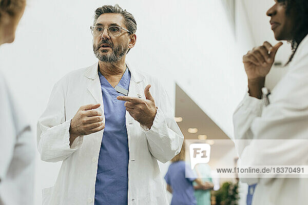 Male physician gesturing while discussing with colleagues at hospital