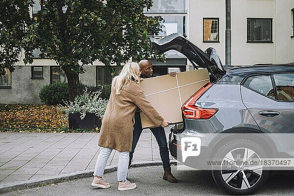 Mann und Frau laden gemeinsam Karton in den Kofferraum eines Autos