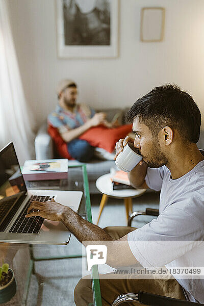 Side view of man drinking coffee while using laptop at home