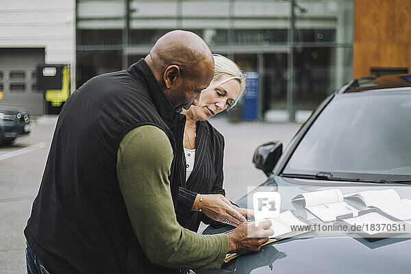 Verkäuferin  die einem männlichen Kunden hilft  während sie in der Nähe des Autos stehend Papierkram erledigt